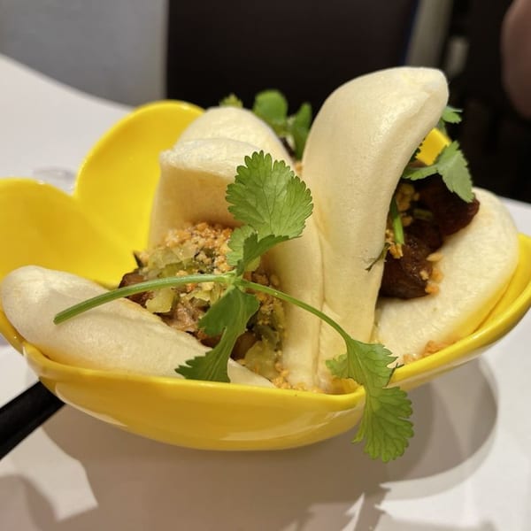 Taiwanese pork belly bao buns with cilantro and crushed peanuts in a yellow dish.