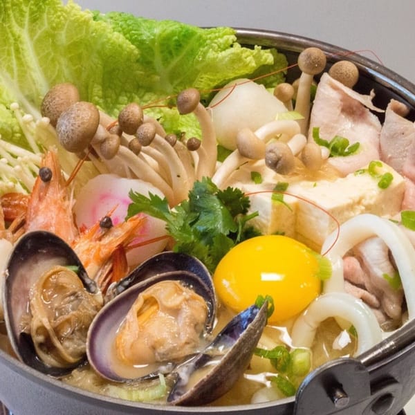 Taiwanese hot pot with seafood, mushrooms, cabbage, tofu, and an egg yolk in a dark pot.