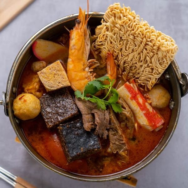 Taiwanese hot pot with shrimp, noodles, meat, tofu, and other ingredients in a rich broth.